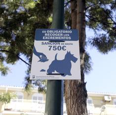 Un cartel avisa de la multa por no retirar las heces de los perros en una calle de Málaga.