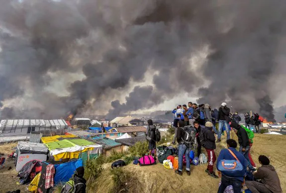Un grupo de inmigrantes visualizan los incendios en el campamento improvisado de Calais. :: P. HUGUEN / afp