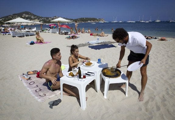 Un empleado temporal de la hostelería sirve una comida a unas turistas en una playa del Mediterráneo. :: jaime reina