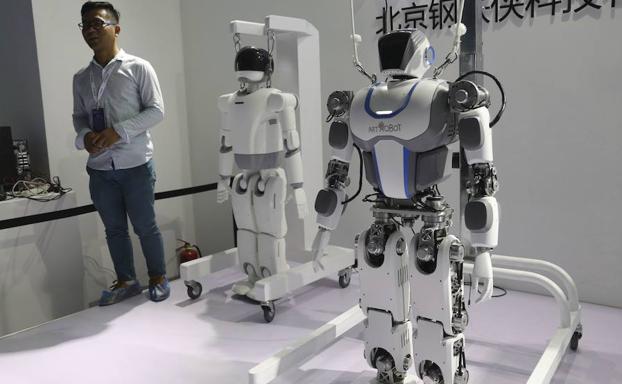 Un visitante posa junto a dos robots durante la Feria Mundial de Robots en Pekín.