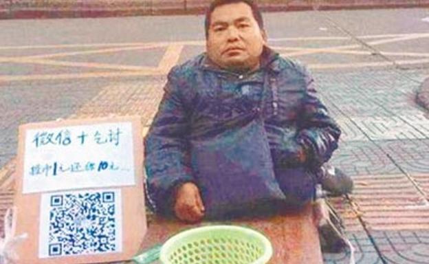 Un vagabundo pide limosna en la calle junto a un cartel con el código QR.