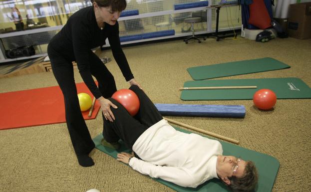 Una instructora ayuda a realizar ejercicios de rehabilitacion dirigidos a personas aquejadas de enfermedades degenerativas.