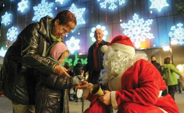 Un Papa Noel entrega un regalo a una niña a las puertas de unos grandes almacenes.