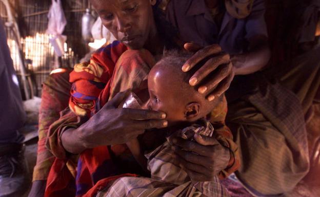 Un niño etíope bebe agua en brazos de su madre.