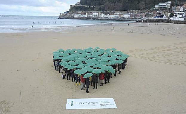 Varias personas forman una flecha en la playa de la Conche el Día Mundial contra el Cáncer.