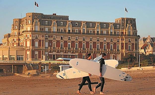 Dos surfistas caminan por la playa de Biarritz frente al Hotel du Palais, que acogerá las sesiones principales del próximo G-7.