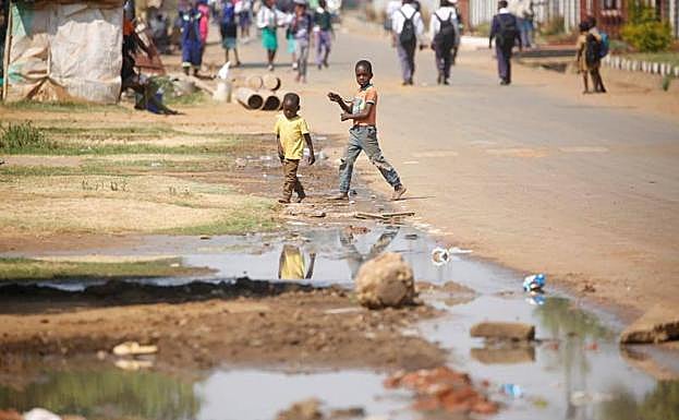 Niños descalzos caminan junto a un río de aguas residuales en Harare, Zimbabue.