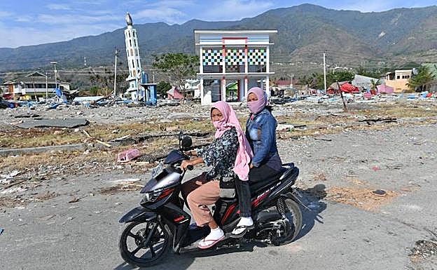Dos mujeres pasan con su motocicleta por Palu. 