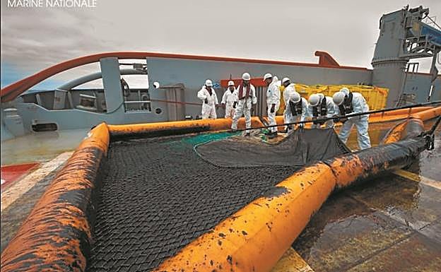 Miembros del buque 'Argonaute' retiran la malla manchada con el combustible que flota en el agua. 