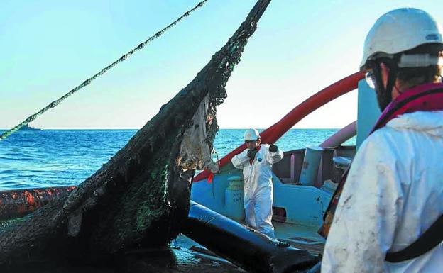 Operarios elevan una barrera cargada de fuel. 