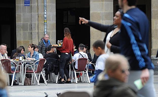 Una camarera atiende una terraza llena de turistas en Donostia.