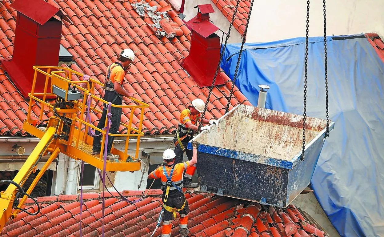 Varios operarios, con un contenedor de obra en el tejado del edificio derrumbado.