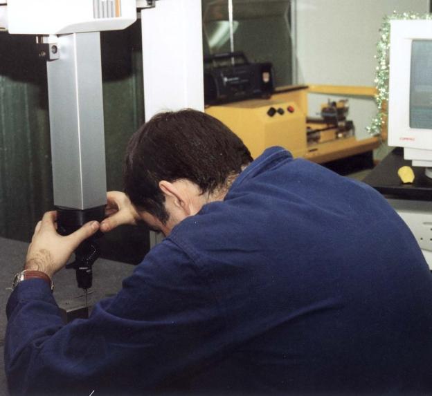Un joven trabaja en una máquina de soldadura y de metrología tridimensional junto a un ordenador.