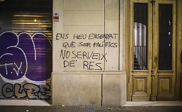 Imagen principal - Arriba, una pintada en una calle de Barcelona. Abajo, operarios tratan de reparar los destrozos en una tienda. 