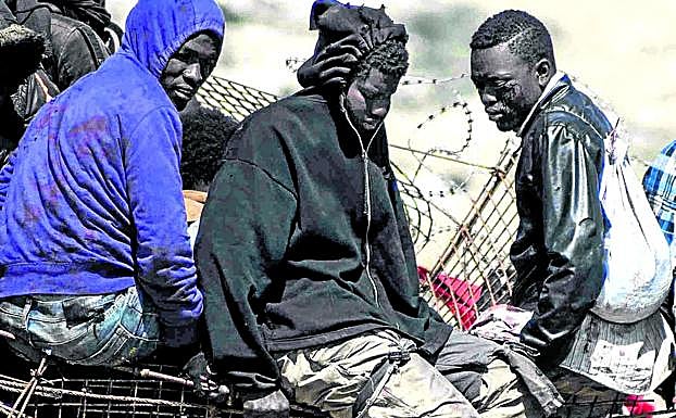 Un inmigrante encaramado en una valla fronteriza muestra sus pies ensangrentados.