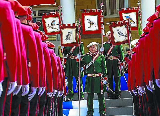 Ertzainas vestidos de gala sostienen los estandartes con aves en un acto ceremonial. 