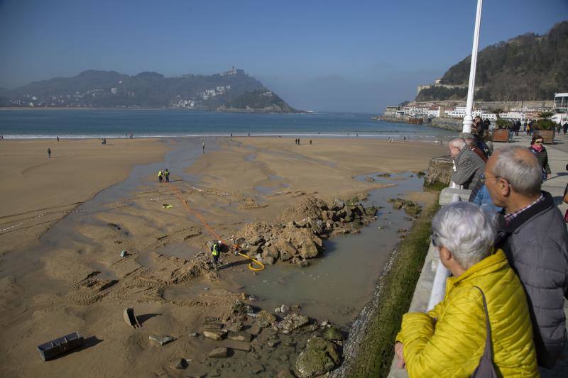 La playa de La Concha se ha convertido en la bajamar de este lunes por la mañana en un inesperado yacimiento arqueológico. La presencia de una pequeña excavadora retirando piedras y escombros junto al muro de costa a la altura del edificio consistorial ha suscitado una gran expectación entre los numerosos viandantes y turistas que han provechado el buen tiempo para dar un paseo. La máquina profundizaba en la arena en busca de los restos de un barco hundido del que hay constancia documental desde el siglo XVIII. 