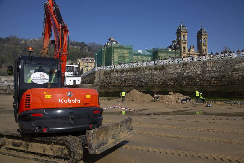 La playa de La Concha se ha convertido en la bajamar de este lunes por la mañana en un inesperado yacimiento arqueológico. La presencia de una pequeña excavadora retirando piedras y escombros junto al muro de costa a la altura del edificio consistorial ha suscitado una gran expectación entre los numerosos viandantes y turistas que han provechado el buen tiempo para dar un paseo. La máquina profundizaba en la arena en busca de los restos de un barco hundido del que hay constancia documental desde el siglo XVIII. 