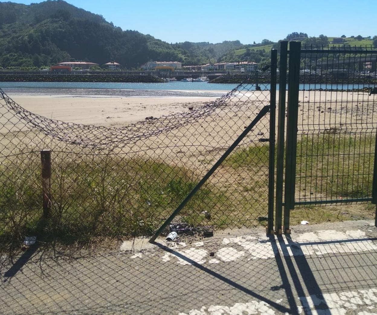 La playa vallada, pero con la valla rota en un tramo. 
