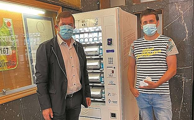 Carlos Abad, a la izquierda, ante la máquina expendedora de mascarillas. 