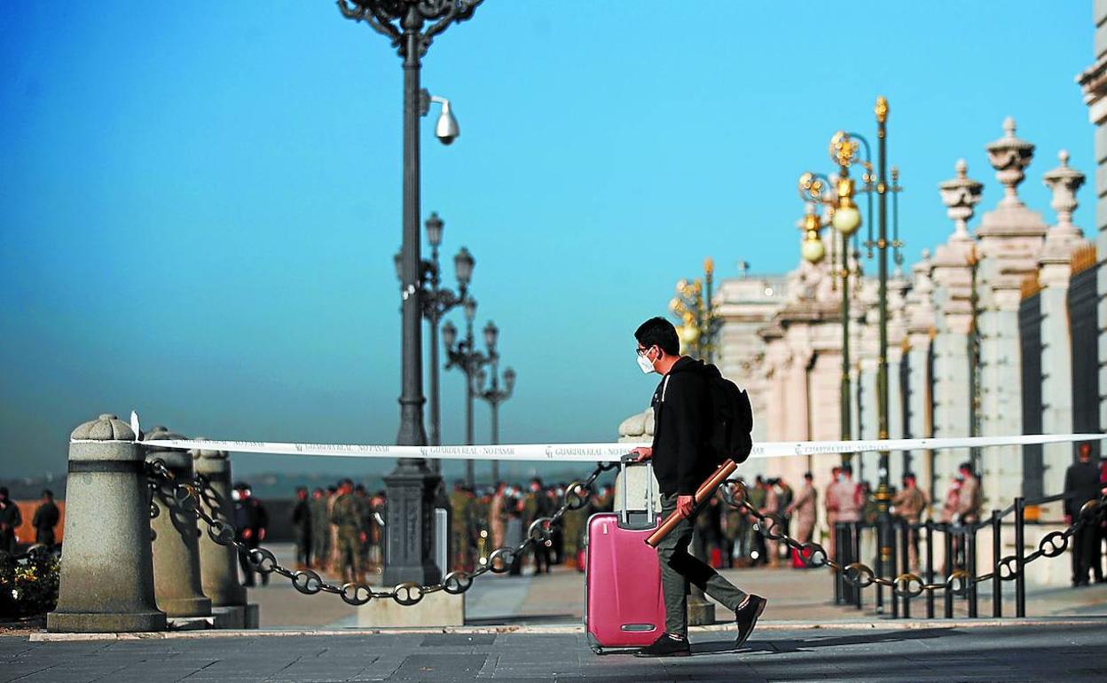 Un joven con su maleta pasa ante el Palacio Real en Madrid, donde ayer el Gobierno español aprobó la declaración del estado de alarma para evitar la expansión del coronavirus.
