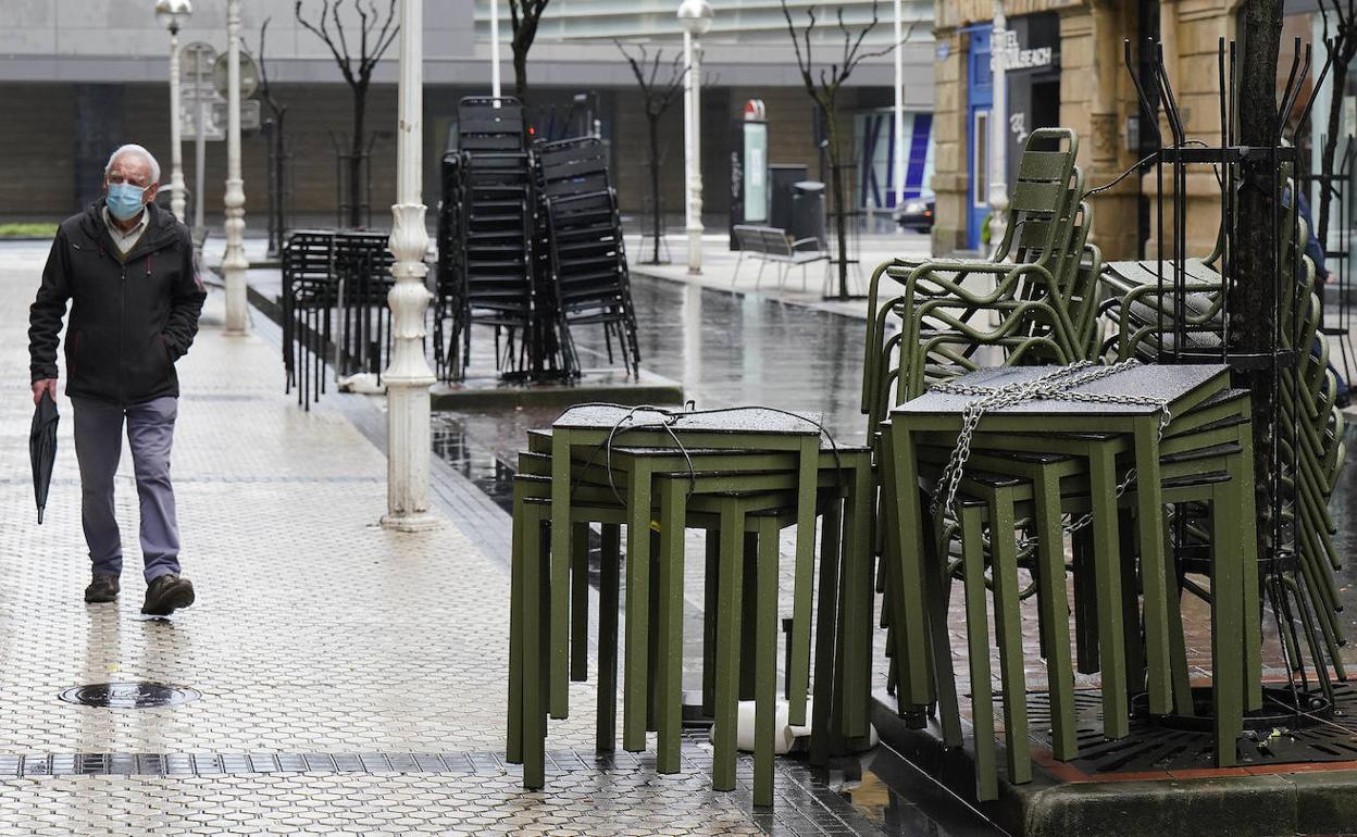 Un hombre camina junto a una terraza recogida en Donostia, donde la hostelería permanece cerrada. 