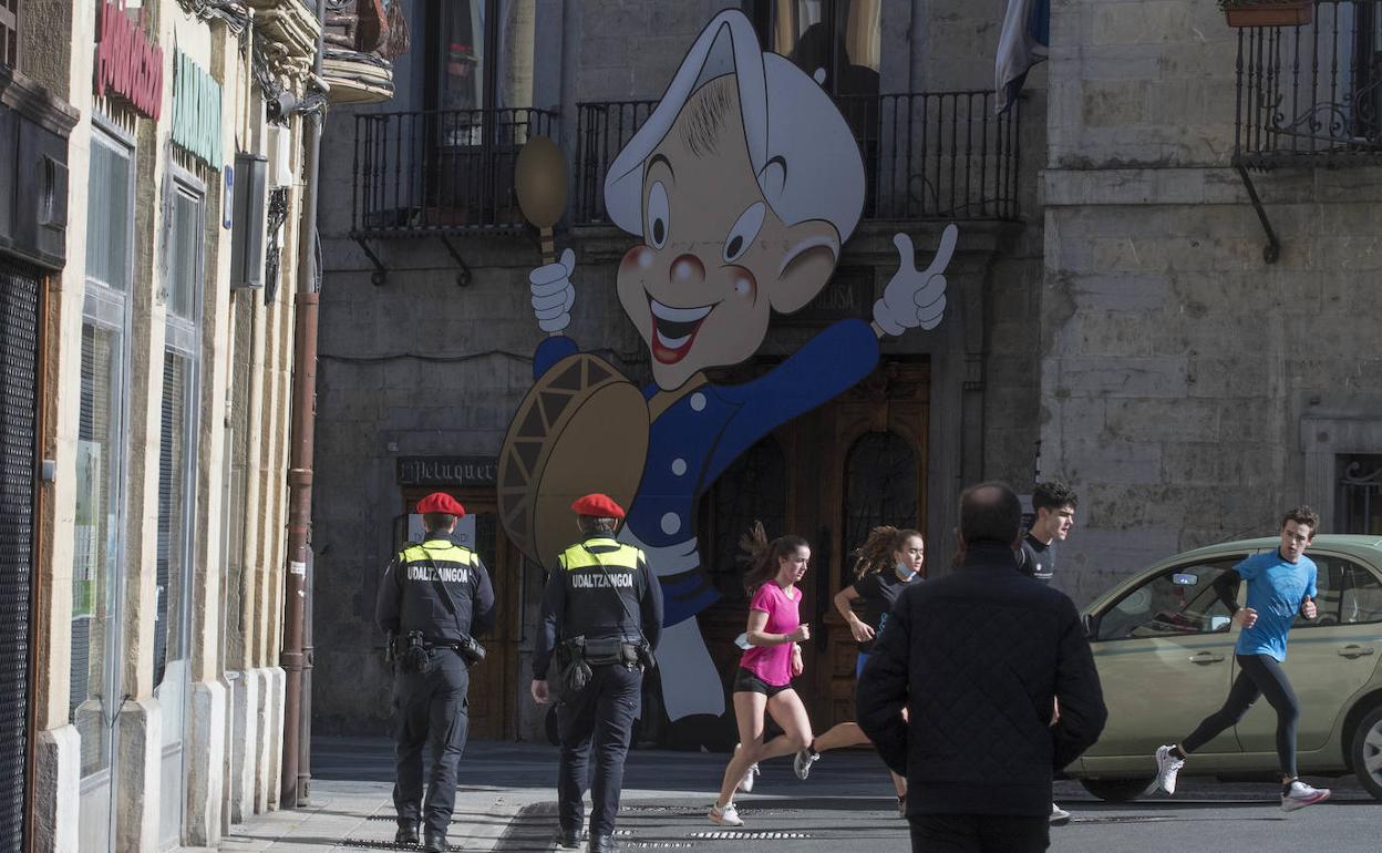 Guardias municipales patrullan por el casco viejo de Tolosa mientras dos jóvenes practican deporte. 