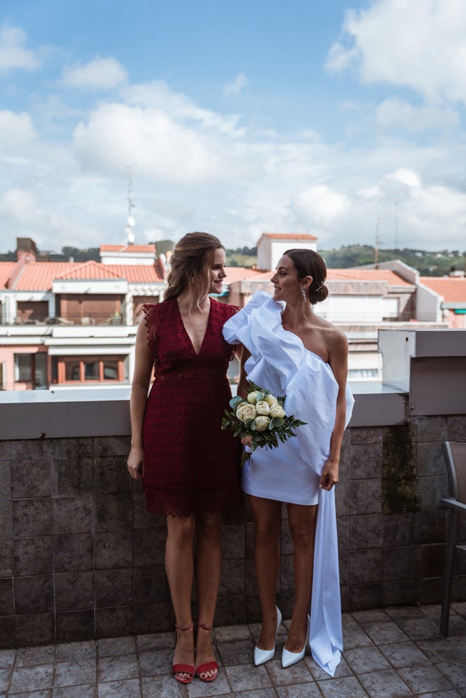 María y Jorge se casaron en Gorliz en una ceremonia íntima adaptada a las circunstancias. De largura 'mini' por encima de la rodilla, con corte asímetrico, volumen en la parte superior y lazadas laterales, la protagonista se ha convertido en una de las novias más impresionantes de las últimas semanas. El diseño lo ha firmado Fabio Encinar, uno de los diseñadores con sede en Madrid más de moda. En cuanto al peinado, otro de los elementos más destacados del estilismo, ha optado por un acertado moño bajo de bailarina súper pulido y tirante, con horquillas de Oui Novias