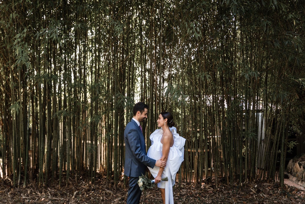 María y Jorge se casaron en Gorliz en una ceremonia íntima adaptada a las circunstancias. De largura 'mini' por encima de la rodilla, con corte asímetrico, volumen en la parte superior y lazadas laterales, la protagonista se ha convertido en una de las novias más impresionantes de las últimas semanas. El diseño lo ha firmado Fabio Encinar, uno de los diseñadores con sede en Madrid más de moda. En cuanto al peinado, otro de los elementos más destacados del estilismo, ha optado por un acertado moño bajo de bailarina súper pulido y tirante, con horquillas de Oui Novias