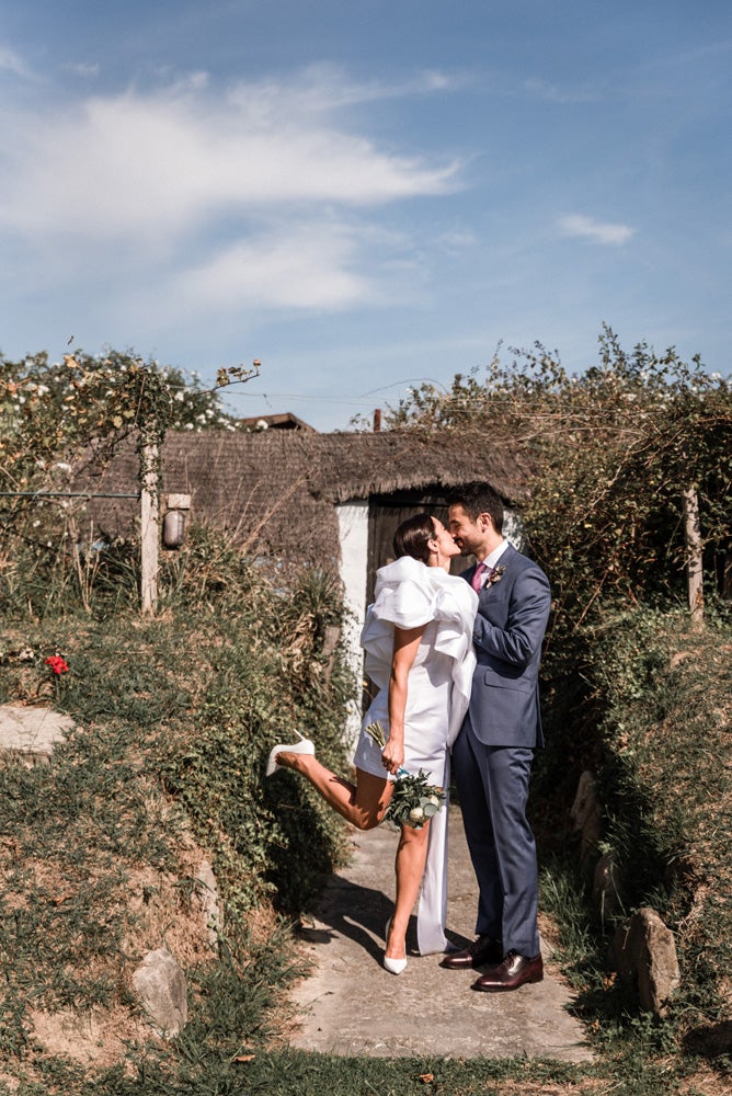 María y Jorge se casaron en Gorliz en una ceremonia íntima adaptada a las circunstancias. De largura 'mini' por encima de la rodilla, con corte asímetrico, volumen en la parte superior y lazadas laterales, la protagonista se ha convertido en una de las novias más impresionantes de las últimas semanas. El diseño lo ha firmado Fabio Encinar, uno de los diseñadores con sede en Madrid más de moda. En cuanto al peinado, otro de los elementos más destacados del estilismo, ha optado por un acertado moño bajo de bailarina súper pulido y tirante, con horquillas de Oui Novias