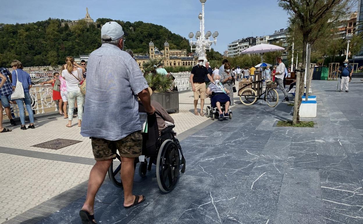 Dos mujeres en silla de ruedas, acompañadas por una persona, se cruzan ayer al mediodíaen el paseo de La Concha de Donostia. 