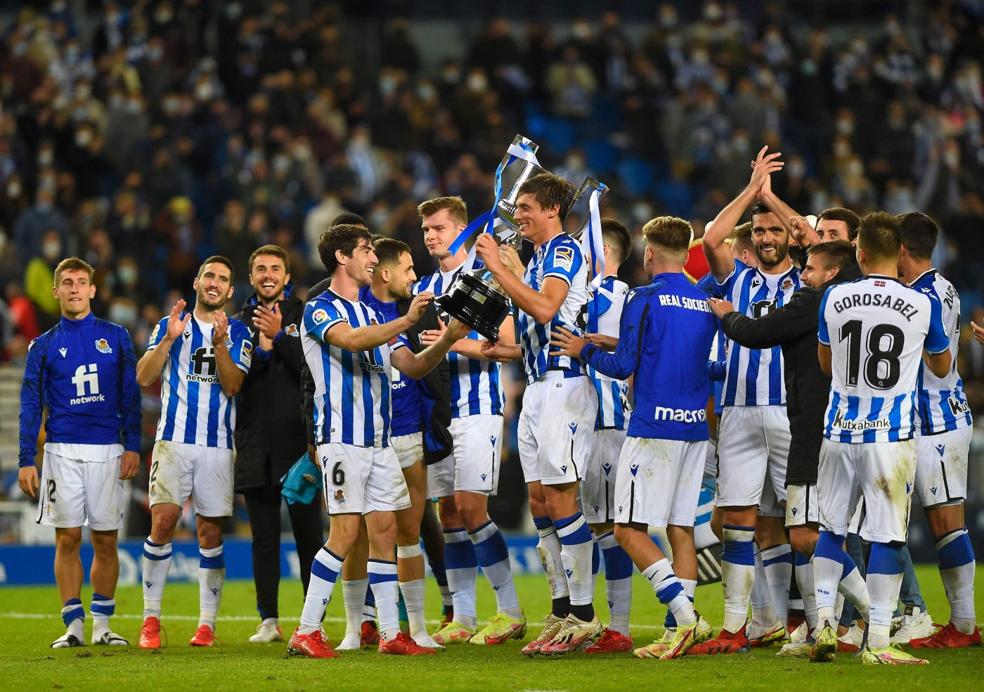 Los jugadores de la Real, felices, celebran junto a la Copa y la afición la victoria conseguida. 