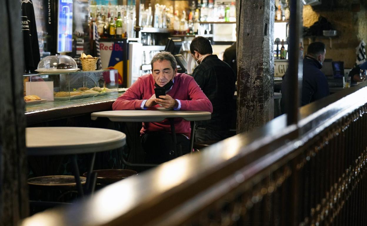 Un cliente mira su teléfono movil en el interior de un local de hostelería. 