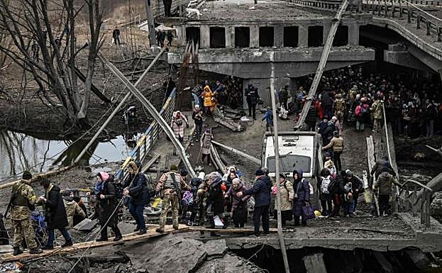 Galería. Soldados ucranianos ayudan a la población a cruzar un puente destruido tras los bombardeos en la ciudad de Irpin.