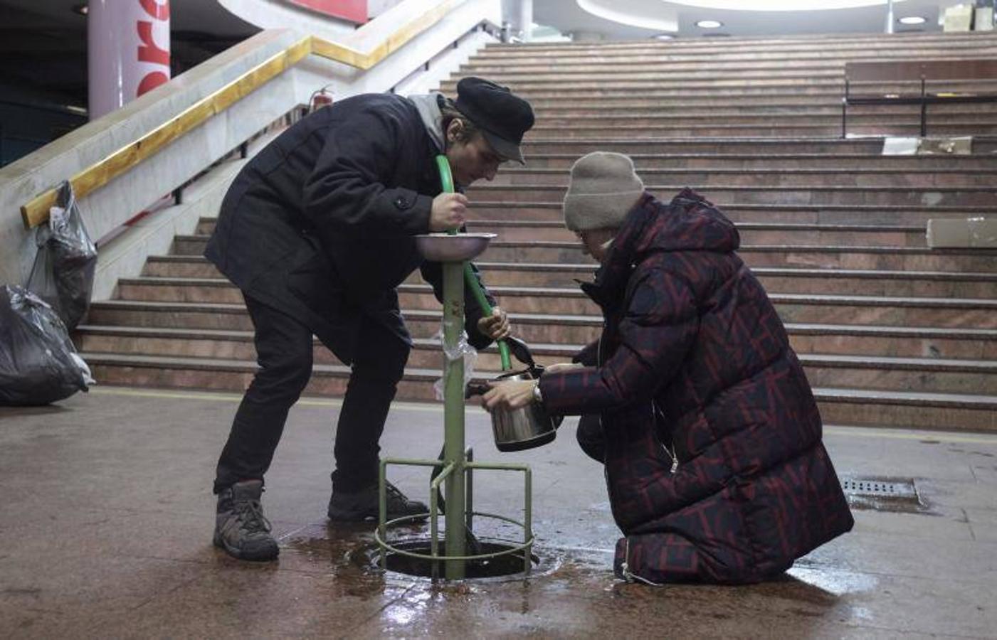 Dos personas tratan de conseguir agua potable dentro del metro de Kiev.