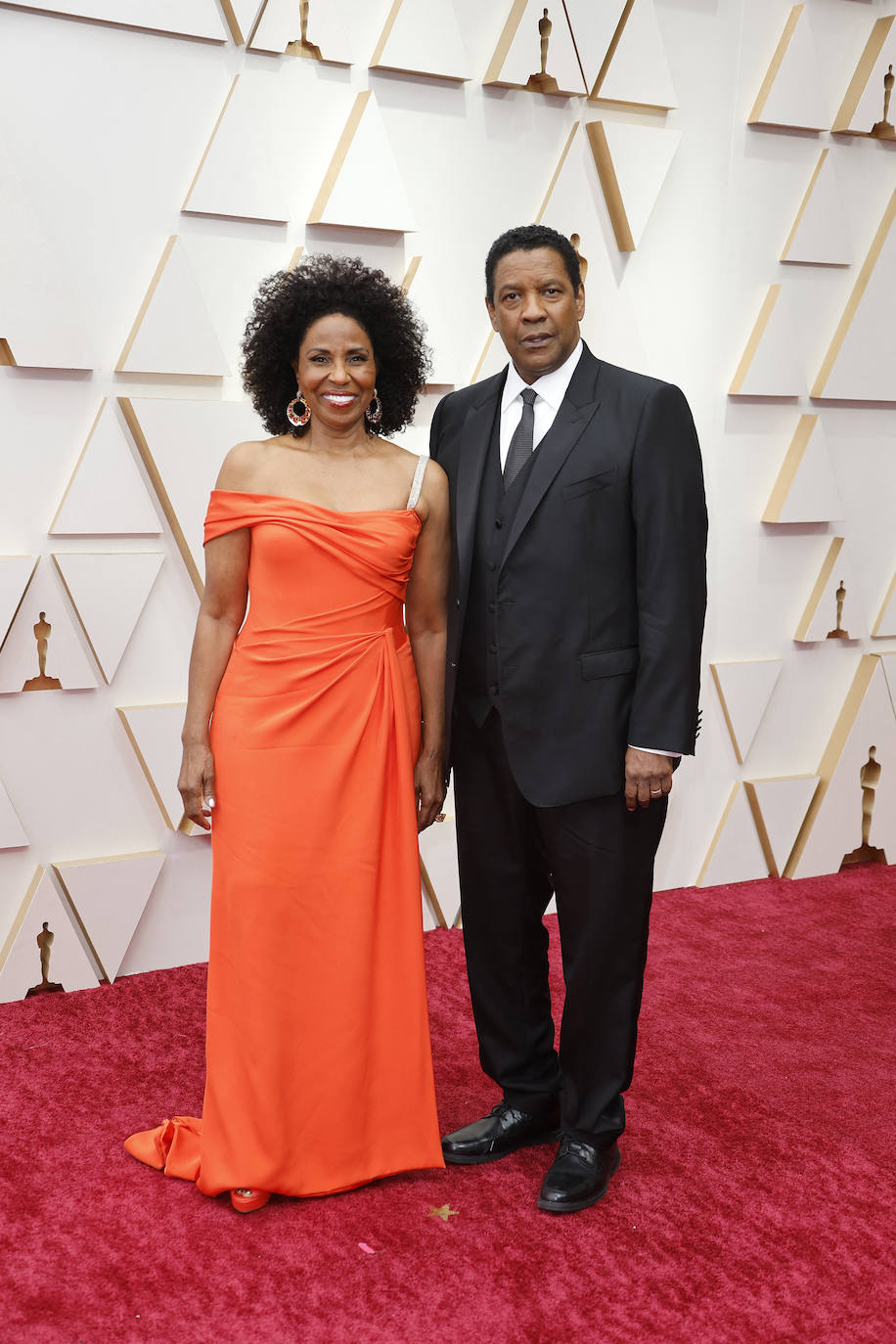 El veterano actor Denzel Washington ha sido de los pocos invitados en lucir corbata en la alfombra roja. Su mujer ha optado por un asimétrico vestido en color naranja, combinado con unas sandalias de plataforma en la misma tonalidad