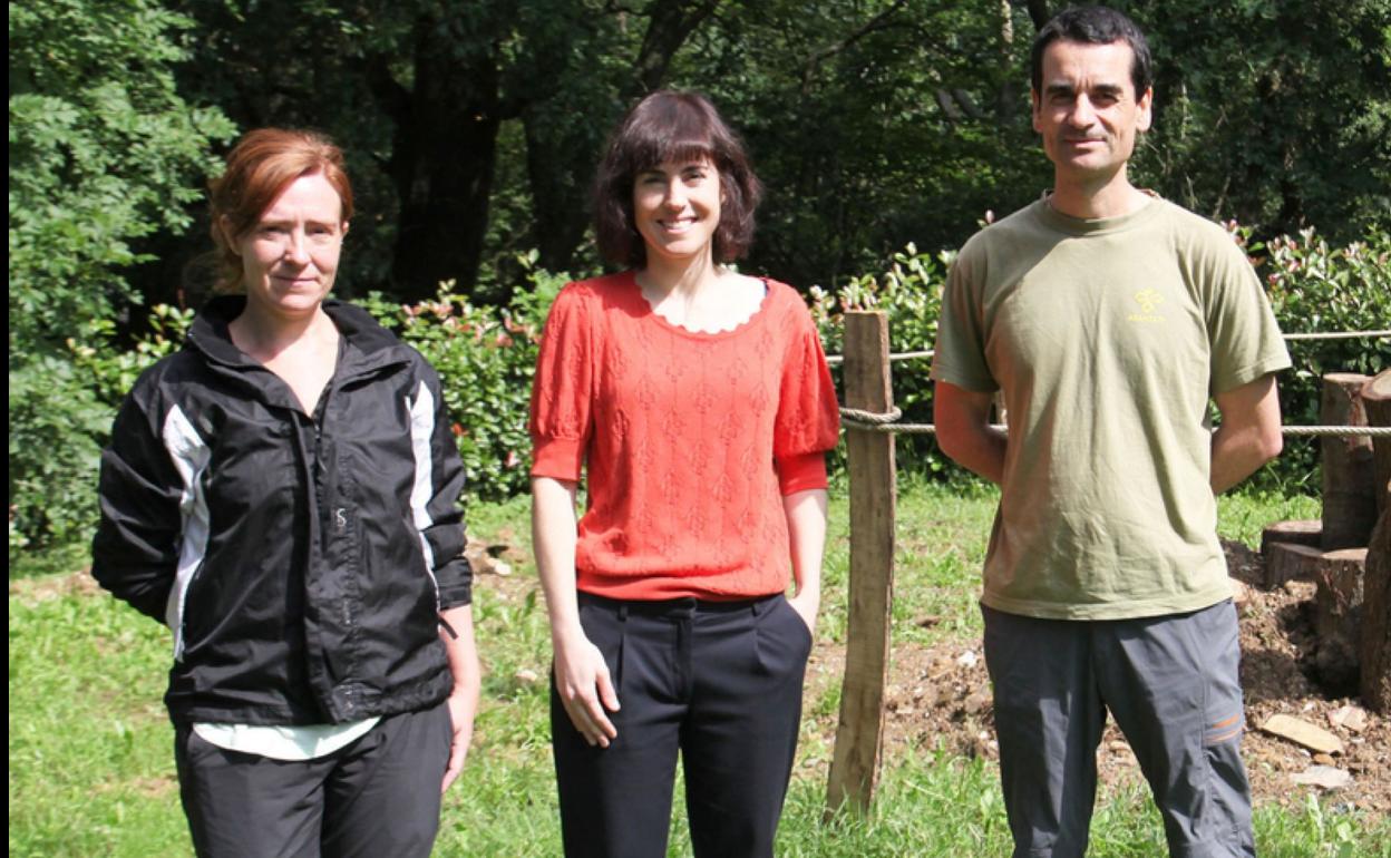 Maitane Alvarez, flanqueada por dos miembros de Aranzadi, delante de un apilamiento de madera. 