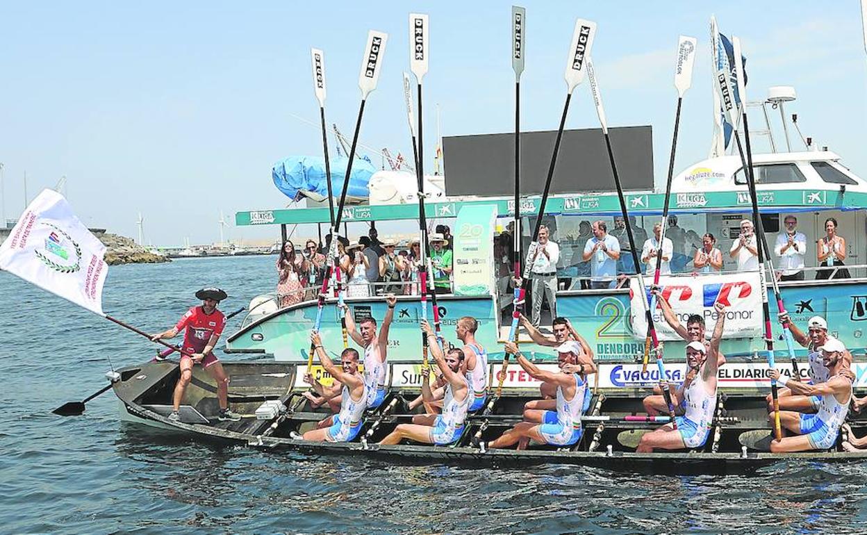 Arkaitz Díaz ondea la Bandera Petronor en la popa de la Torrekua II mientras los remeros levantan sus remos. 
