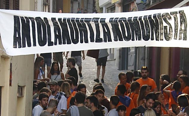 Jóvenes disfrutando de las fiesta de Mutriku debajo de un cartel de 'Antolakuntza Komunista' 