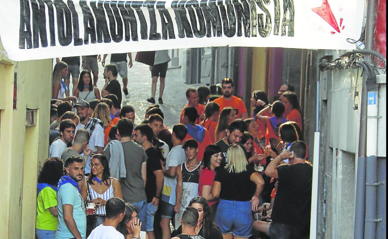 Jóvenes disfrutando de las fiestas de Mutriku debajo de un cartel de Antolakuntza Komunista. 