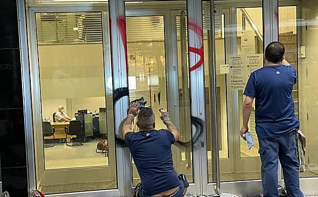 Operarios limpiando las pintadas en una entidad bancaria.