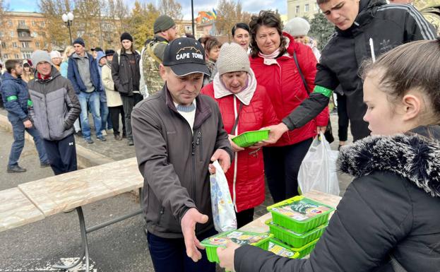 Imagen principal - Reparto de ayuda humanitaria a residentes de la ciudad de Jersón mientras otros cargan sus móviles en generadores. 