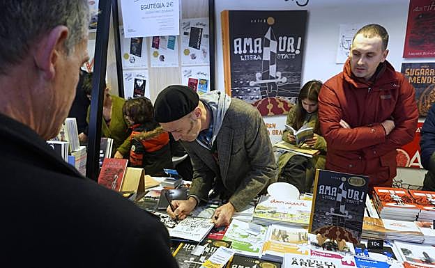 Imagen principal - Asisko Urmeneta firma ejemplares de 'Amaiur! Libera State', una visión ilustrada y muy documentada de lo que ocurrió en Amaiur. Harkaitz Cano y Oier Aranzabal en el stand del colectivo Zart!, atendiendo a visitantes ilustres. El geógrafo y profesor japonés Ishii Hisao presentó ayer su tesis sobre Durangoko Azoka.