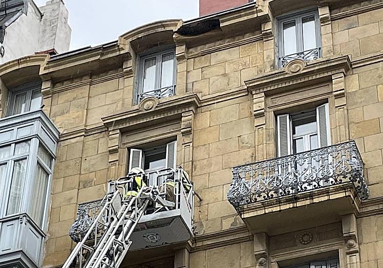 Los bomberos trabajan en el balcón afectado del cuarto piso de la calle Urbieta mientras que se puede ver el hueco que ha dejado la cornisa desprendida.