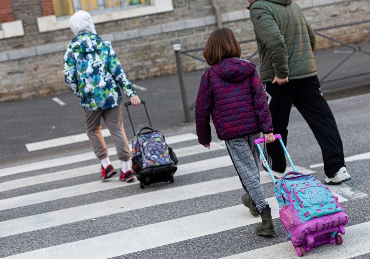 Un par de escolares que tiran de sus mochilas con ruedas cruzan la calle para acceder a su colegio.