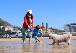 Un niño juega con su madre y un perro en la playa de La Concha