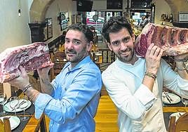 Los hermanos Aritz Eder y Gorka Petralanda sostienen dos grandes piezas de chuleta en su conocido restaurante.