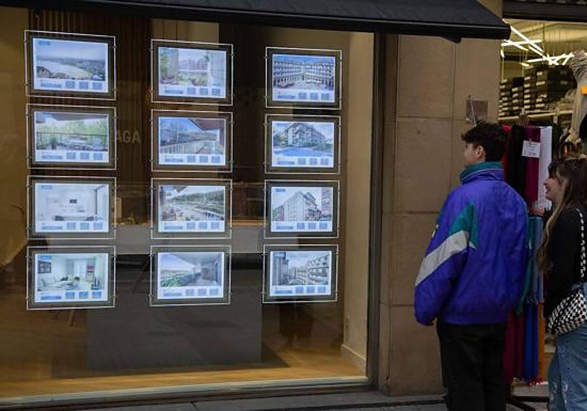 Dos jóvenes observan el escaparate de una imobiliaria donostiarra.