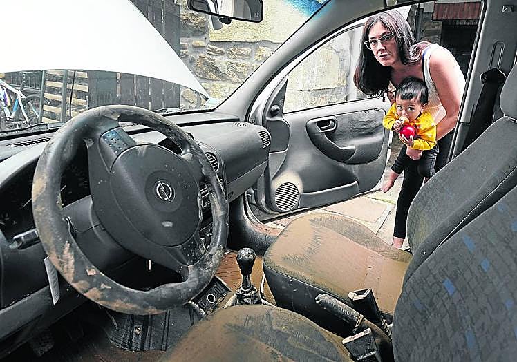 Imagen principal - Eluska, hija de Coro, se asoma a su coche junto al pequeño Janur. El agua entró hasta los asientos y ahora, además del barro, el motor no arranca; Xuban señala el lugar donde el monte se desprendió, justo detrás de la casa donde vive su pareja, Leyre, con su familia en Lesaka y Edurne y Karlos terminan de limpiar la consulta de fisioterapia de este último, que hoy tiene que abrir porque tiene citas desde las 9.00 horas. 