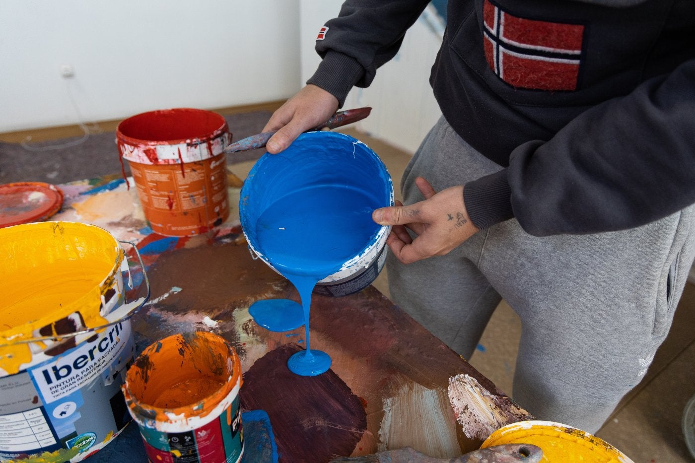 Imagen secundaria 2 - Arriba, Nexgraff da los últimos retoques a uno de sus murales. En medio, la escuela pública dde Villabona cuenta con dos murales de Nexgraff. Debajo, Nexgraff con un bote de pintura azul.